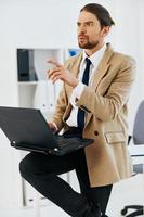 man in beige jacket in the office with a laptop executive photo