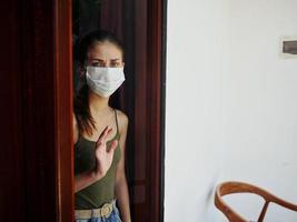 trastornado mujer en médico máscara mirando fuera el ventana prohibición encierro foto