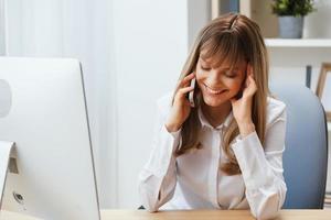 sonriente contento adorable rubia mujer de negocios trabajador persona de libre dedicación hablando con cliente en llamada en ligero moderno oficina. disfruté empleado trabajo en computadora en línea en apoyo servicio. Copiar espacio foto