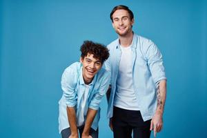 pelo rizado chico en un azul camisa inclinado adelante y un rubio hombre en un azul antecedentes amigos foto