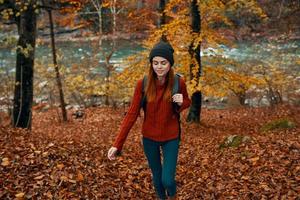 woman in a sweater with a backpack resting in a park near the river in nature in autumn photo