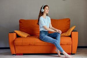 hermosa mujer sentado en el sofá a hogar escuchando a música en auriculares estilo de vida foto