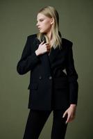 A blonde lady holds a jacket by the collar with one hand posing on a green background in the studio. A concept for clothing brands. Cool offer for fashionable suits photo