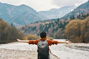 happy woman in the mountains travels near the river in nature and raised her hands up photo