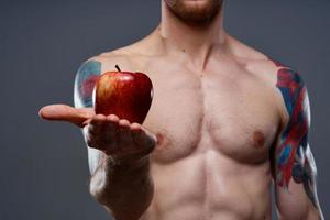 tattooed athlete holding red apple on gray background naked torso cropped view photo