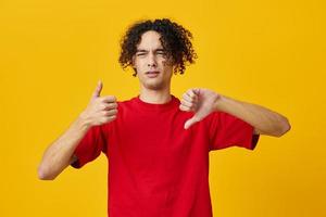 Dissatisfied funny Caucasian young man in red t-shirt show Dis Like gesture posing isolated on yellow studio background. The best offer with free place for advertising. Emotions for everyday concept photo