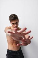 A man with a naked torso gestures with his hands in front of his face against a light background cropped view photo