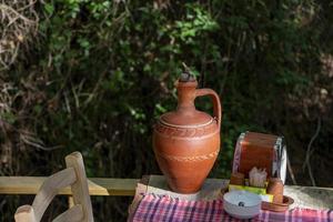 The clay jug on a wooden table in the garden. Traditional handmade clay jug. Vintage style. photo