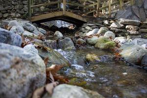 Wooden bridge over a small stream in the forest. Waterfall in the garden with rocks and leaves in the autumn season. Wooden bridge over a stream in the garden of a country house photo