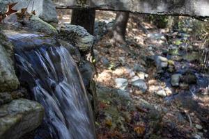 Waterfall in the autumn forest with fallen leaves on the rocks. Small waterfall in the forest. Mountain landscape. photo