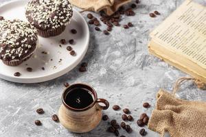 Roasted coffee beans in cup and cake on grey textured background photo