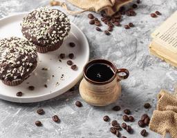 Roasted coffee beans in cup and cake on grey textured background photo