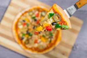 Close up and top view of Chicken mushroom jalapeno pizza slice lifted from wooden cutting board. photo