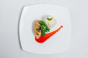 Pan roasted chicken breast with long green beans and light vegetable rice platter. Food decorating with red sauce on a white plate. Isolated white background. photo