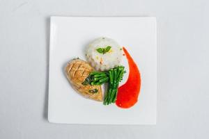 Pan roasted chicken breast with long green beans and light vegetable rice platter. Food decorating with red sauce on a white plate. Isolated white background. photo