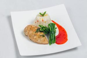 Pan roasted chicken breast with long green beans and light vegetable rice platter. Food decorating with red sauce on a white plate. Isolated white background. photo