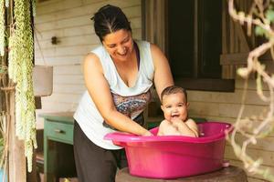 Mother bathes her daughter in washbowl outdoor. A loving relationship between a mother and baby photo