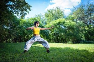 Woman practices Tai Chi outdoor, provides additional health benefits, such as exposure to the sun for vitamin D production and connection with nature to reduce stress and improve emotional well-being. photo