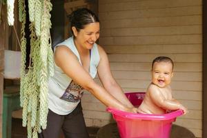 un bebé se baña con su madre en el jardín. él tiene un lote de divertido y disfruta el agua en un caliente día. foto