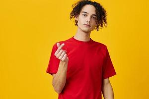 Lovely funny Caucasian young man in red t-shirt show heart shape gesture posing isolated on over yellow studio background. The best offer with free place for advertising. Emotions for everyday concept photo