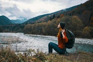 woman near the river in the mountains with a backpack on her shoulders are resting in the autumn forest photo