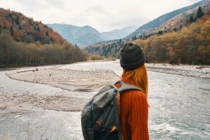 beautiful traveler with a backpack near the river in the mountains on nature landscape photo