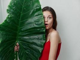 surprised woman in red swimsuit holding green large leaf in hands cropped view close-up photo