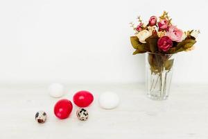 painted Easter eggs and a bouquet of flowers in a vase on a light table photo