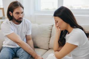 An Asian woman is sad and crying with her male friend at home. Stress and misunderstanding in a relationship between two people and supporting each other's mental and emotional well-being photo