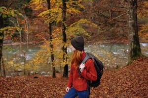 side view of happy woman in park in autumn near river and backpack on her back photo