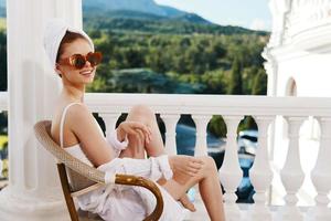 sensual y hermosa mujer en Gafas de sol se sienta en un abierto balcón relajación concepto foto