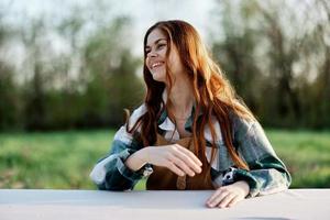 A beautiful woman laughs with a toothy smile and enjoys lounging in a green park on a summer evening in the setting sunlight. The concept of a healthy lifestyle and the bati of self-care photo