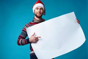 Cheerful man in a santa hat holding a banner holiday blue background photo