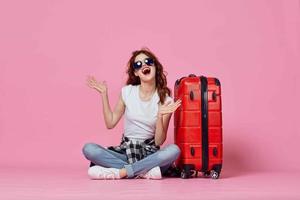 cheerful pretty woman with red suitcase passport and plane ticket travel pink background photo