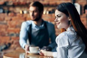 bartender in gray apron sits at the table and client with a cup of coffee brick wall interior model photo