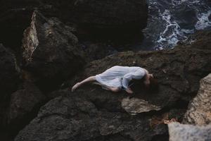 Barefoot woman in a secluded spot on a wild rocky coast in a white dress view from above photo