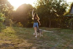 un mujer carreras su espalda a el cámara con un perro en el bosque durante un noche caminar en el bosque a puesta de sol en otoño. estilo de vida Deportes formación con tu amado perro foto