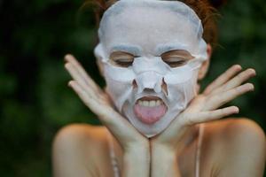Portrait of a woman face mask Show tongue closed eyes skin care bushes in the background photo