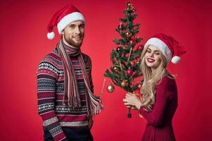 hombre y mujer en pie siguiente a Navidad árbol juguetes estilo de vida rojo antecedentes foto