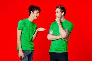 two men in green t-shirts are standing side by side communication photo