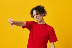 Dissatisfied funny Caucasian young man in red t-shirt show Dis Like gesture posing isolated on yellow studio background. The best offer with free place for advertising. Emotions for everyday concept photo