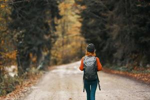 woman with a backpack in a hat and an orange sweater on the road in the autumn forest photo