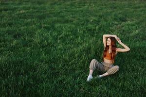 A girl in comfortable clothes sat on the grass after a walk in the park to meditate and rest in the sunlight photo