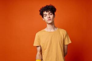 Cheerful curly guy in a yellow t-shirt oranges in his hands red background photo