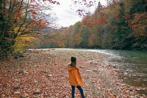 alegre mujer en un amarillo chaqueta cerca el río otoño caminar foto