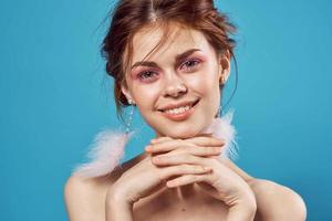 woman with bare shoulders fluffy earrings bright makeup blue background photo