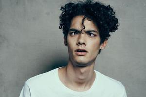 trendy teenager with curly hair in a white t-shirt on a gray background fun emotions photo