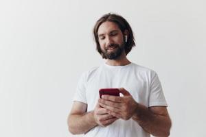 hombre blogger sostiene un teléfono en su manos y comunica con personas en línea en social redes con un sonrisa y un blanco camiseta en un blanco antecedentes foto