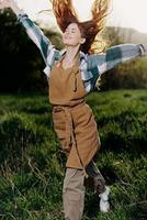 mujer caminando en el césped en naturaleza sonriente en granja ropa con hermosa pelo volador en el viento contento en el rayos de verano puesta de sol ligero foto