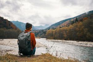 un viajero en un chaqueta con un mochila en su espalda sombrero montañas paisaje río foto